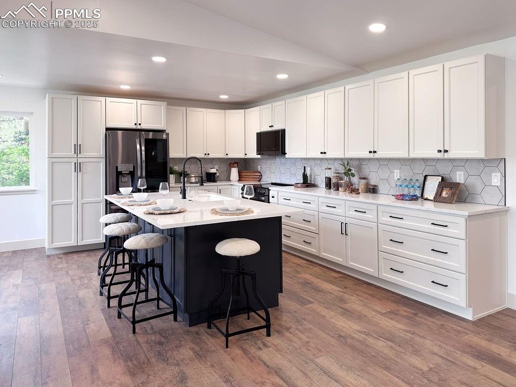 14546 Pine View Road Larkspur, CO 80118 - Photo 5 of 37 Kitchen with black appliances, a kitchen bar, dark wood-style flooring, tasteful backsplash, and white cabinets