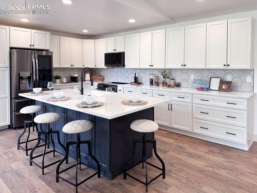 14546 Pine View Road Larkspur, CO 80118 - Photo 6 of 37 Kitchen featuring black appliances, wood finished floors, white cabinets, tasteful backsplash, and recessed lighting