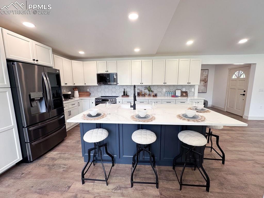 14546 Pine View Road Larkspur, CO 80118 - Photo 7 of 37 Kitchen featuring appliances with stainless steel finishes, a breakfast bar area, tasteful backsplash, white cabinetry, and recessed lighting