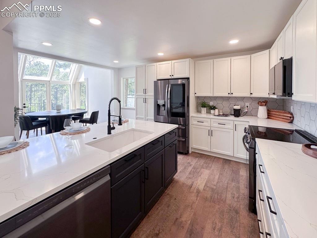 14546 Pine View Road Larkspur, CO 80118 - Photo 8 of 37 Kitchen featuring appliances with stainless steel finishes, white cabinetry, light wood-type flooring, dark cabinets, and decorative backsplash