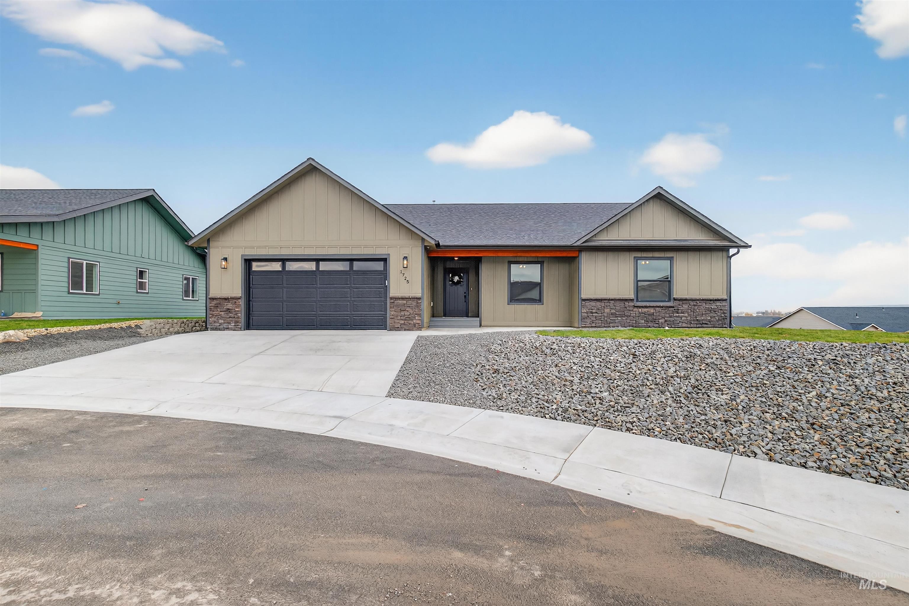 View of front facade with stone siding, driveway, board and batten siding, and an attached garage