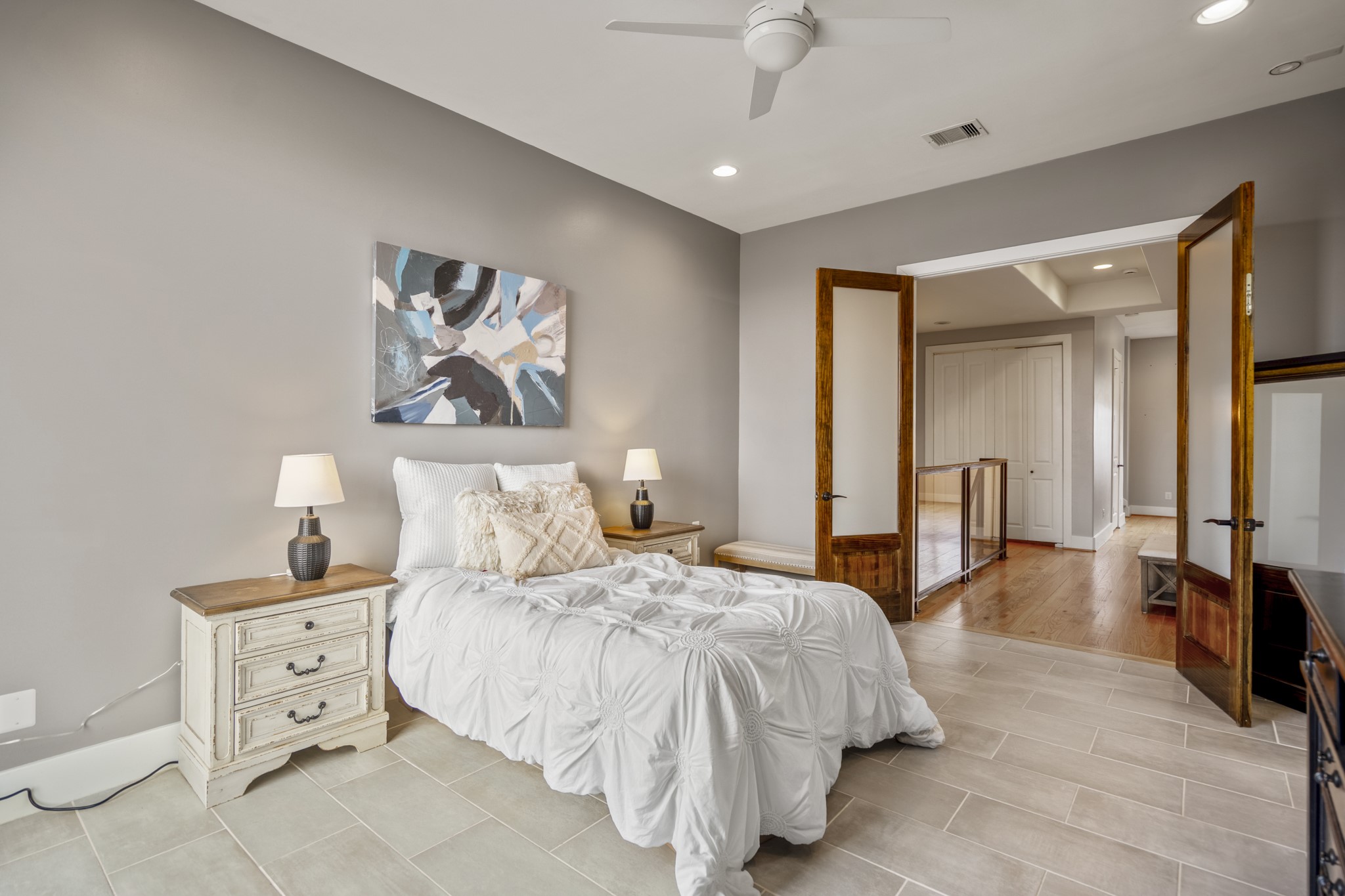 1310 West Dallas Street Houston, TX 77019 - Photo 35 of 50 Stepping back out of the primary bath, the suite opens to the upstairs landing, with tile flooring, a ceiling fan, and French doors that give the space a quiet, private feel. The landing connects the home’s upper level, overlooking the staircase below and leading seamlessly toward the third-floor study just ahead.