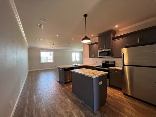 a kitchen with stainless steel appliances granite countertop a refrigerator a sink dishwasher a stove and white countertops with wooden floor