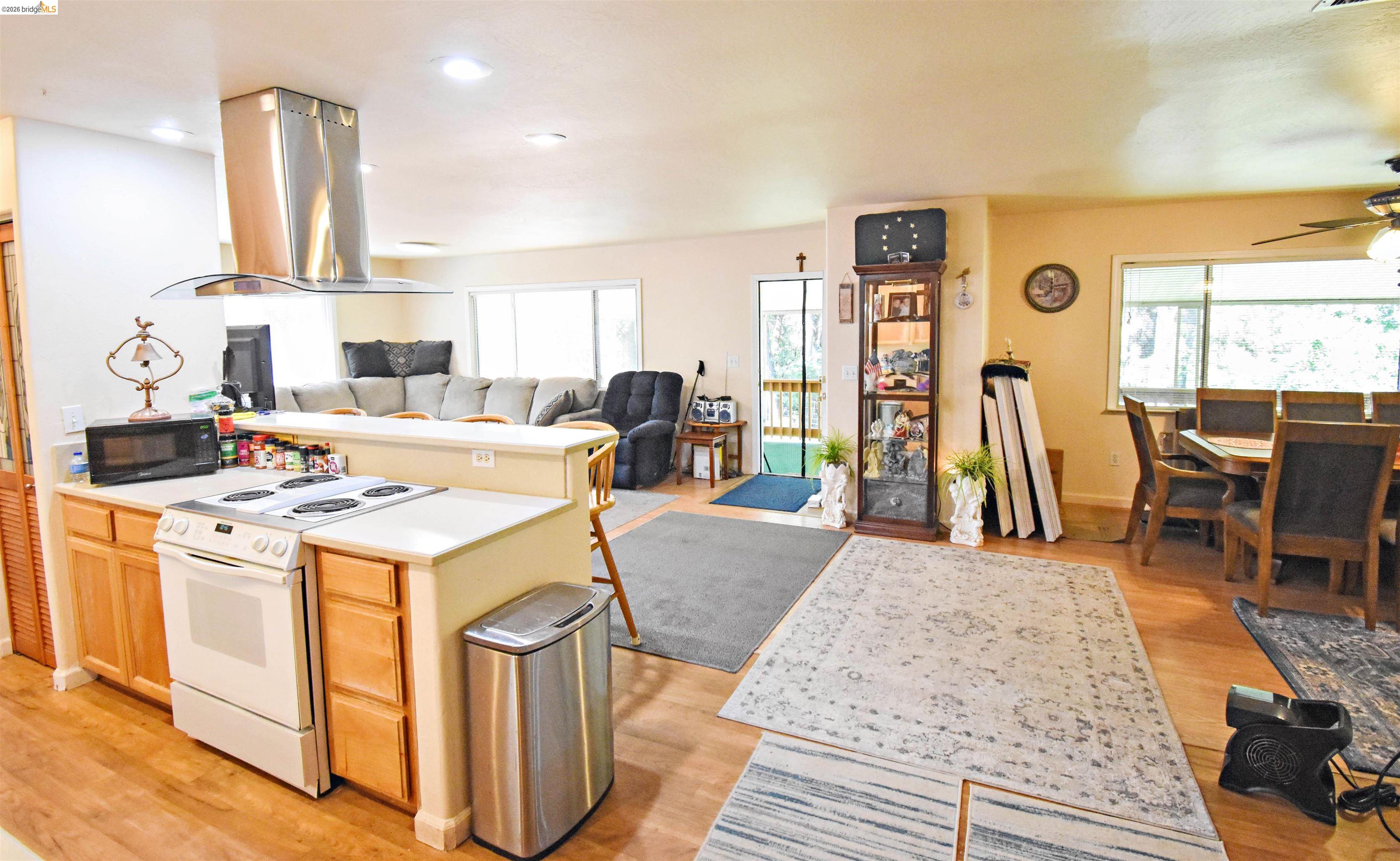 13904 Tuolumne Road Sonora, CA 95370 - Photo 20 of 44 Open-concept living space featuring wood-finish flooring, a kitchen island with integrated range and a stainless steel range hood, ample natural light from multiple windows, and a dining area with a ceiling fan