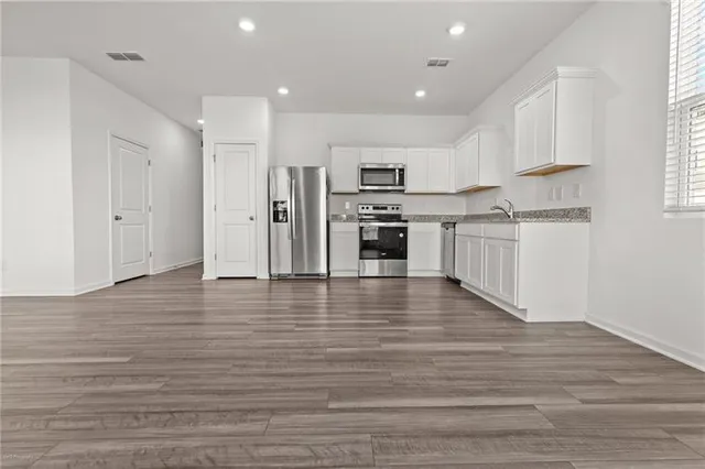 a kitchen with stainless steel appliances granite countertop a stove top oven a sink dishwasher and a refrigerator with wooden floor