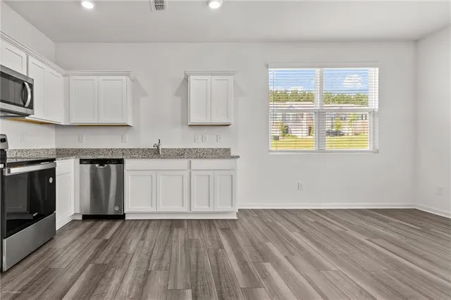 a kitchen with granite countertop wooden floors stainless steel appliances and sink