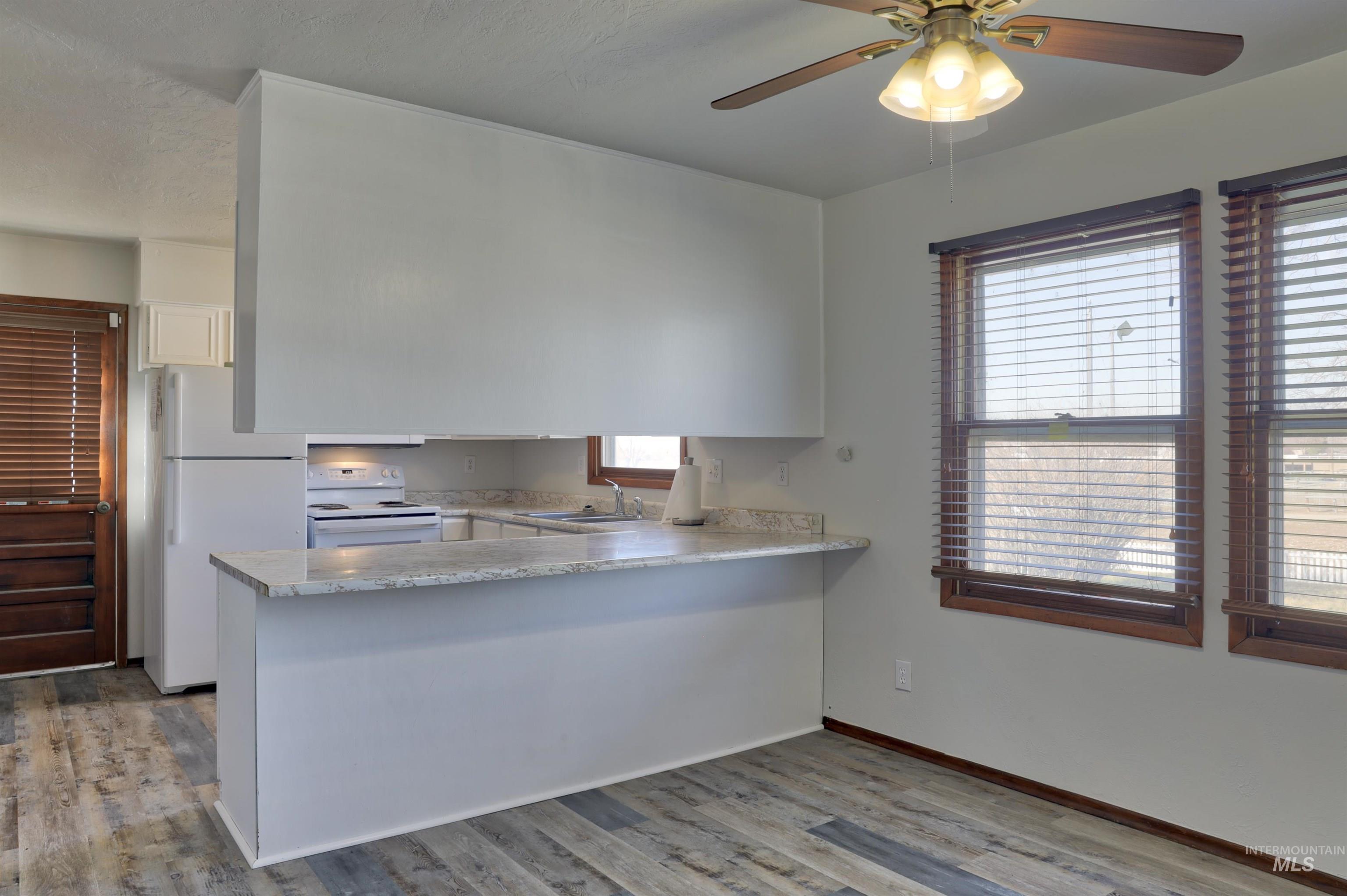 8027 Chuckar Lane Boise, ID 83709 - Photo 7 of 19 Kitchen with white appliances, light wood finished floors, a ceiling fan, a peninsula, and white cabinetry