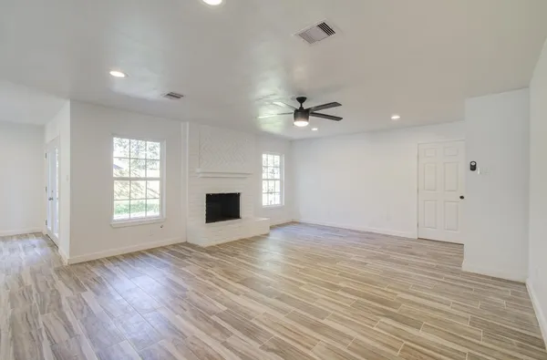 a view of an empty room with wooden floor fireplace and a window
