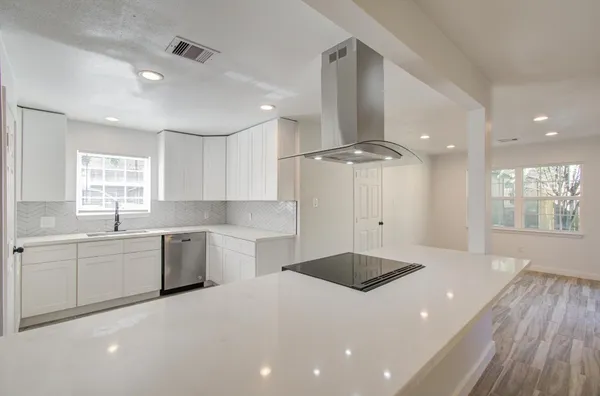 a kitchen with a sink dishwasher a stove and white cabinets with wooden floor