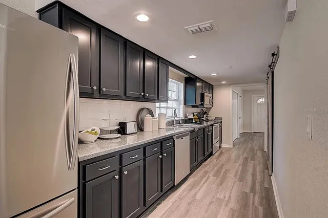 a kitchen with stainless steel appliances granite countertop wooden cabinets a sink dishwasher a stove and a refrigerator with wooden floor