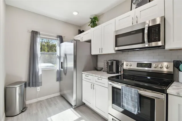 a kitchen with stainless steel appliances granite countertop white cabinets a stove a microwave and a refrigerator