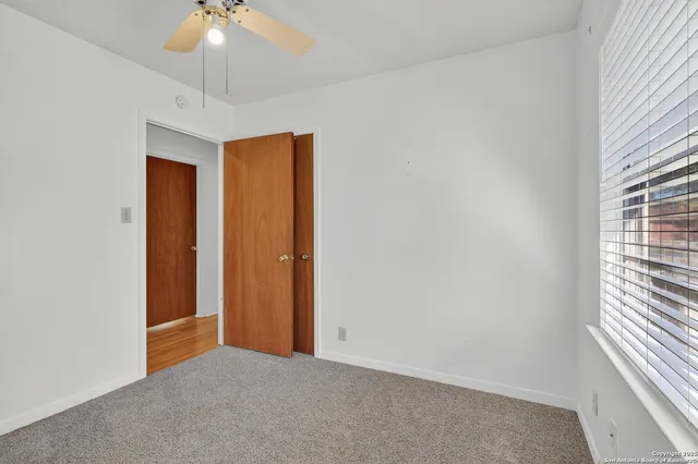 an empty room with a chandelier fan and windows