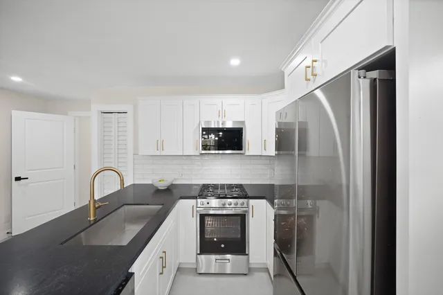 a kitchen with stainless steel appliances granite countertop a refrigerator a stove a sink a microwave a dining table and chairs with wooden floor