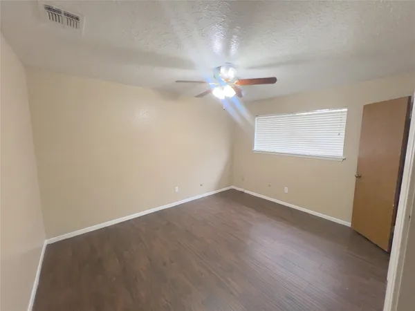 an empty room with wooden floor fan and window