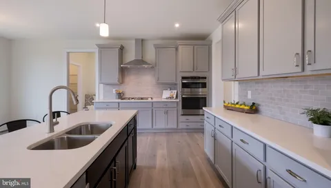 a kitchen with stainless steel appliances sink a stove and white cabinets with wooden floor