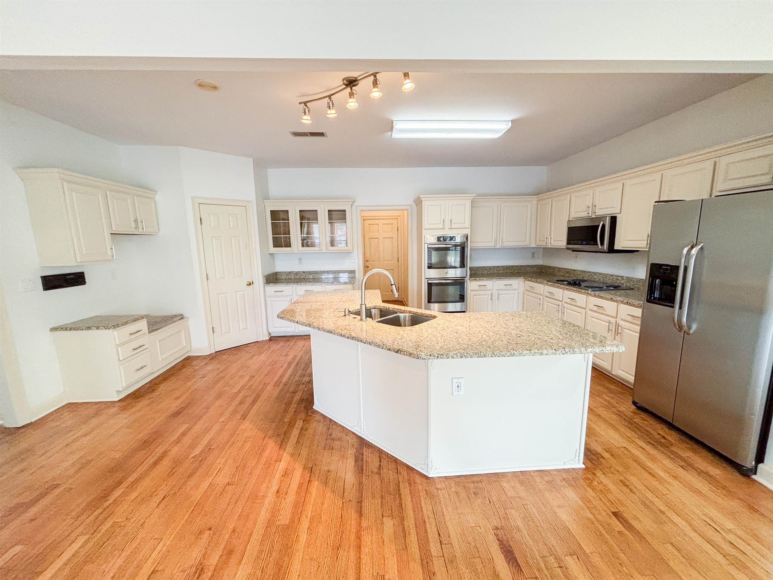 1923 Swynford Lane Collierville, TN 38017 - Photo 12 of 35 Kitchen featuring stainless steel appliances, a kitchen island with sink, light stone countertops, and light wood finished floors