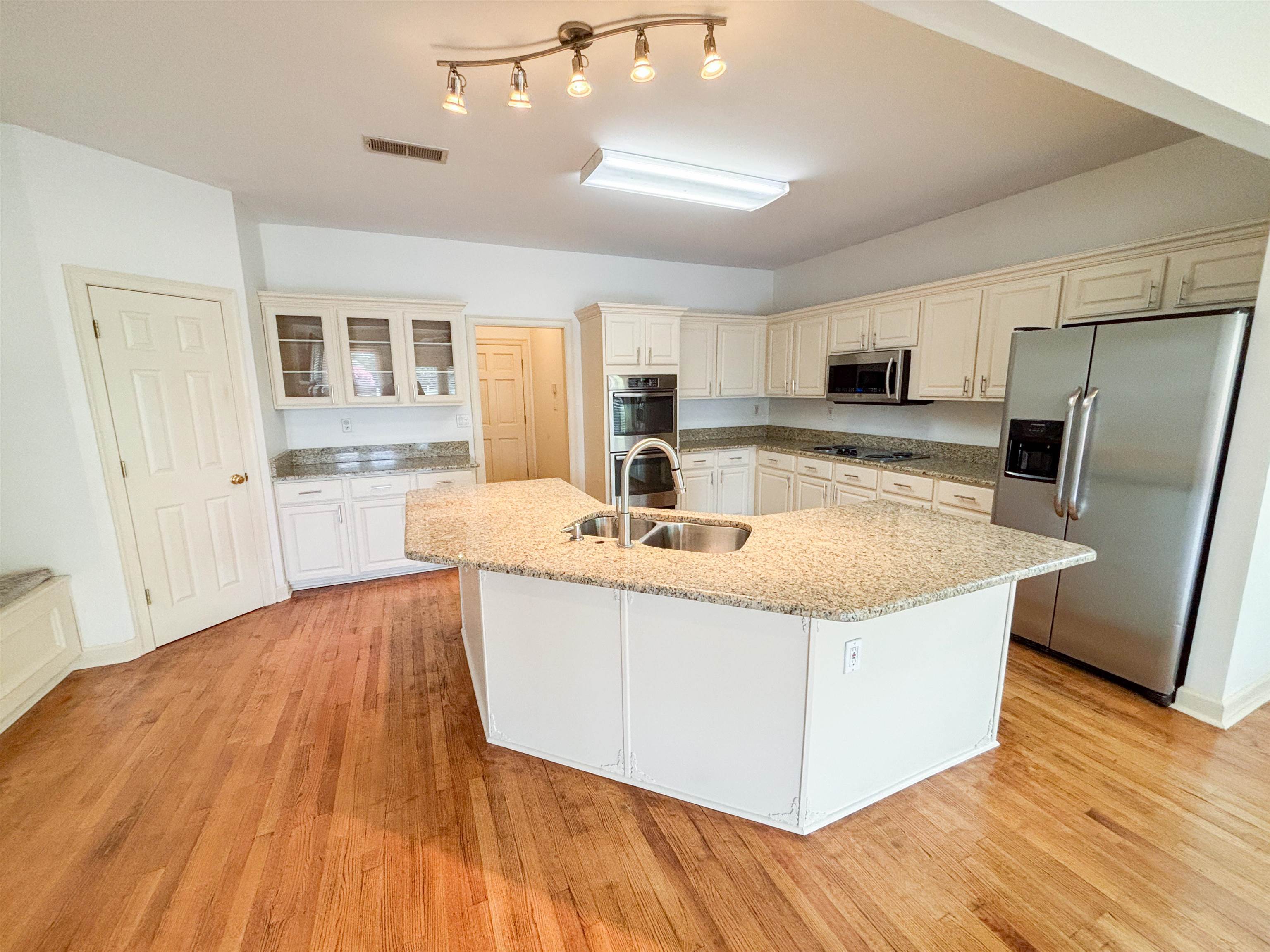 1923 Swynford Lane Collierville, TN 38017 - Photo 13 of 35 Kitchen featuring stainless steel appliances, a center island with sink, light wood finished floors, light stone countertops, and glass insert cabinets