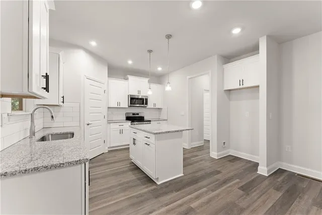 a large kitchen with stainless steel appliances granite countertop a stove a sink a refrigerator and white cabinets with wooden floor