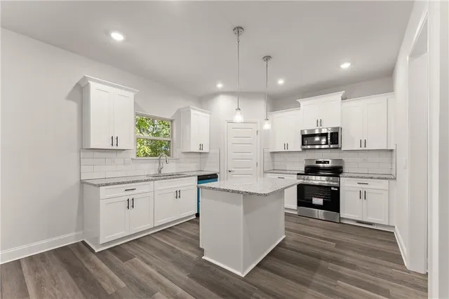 a large kitchen with granite countertop a stove top oven a sink a counter space and wooden floor