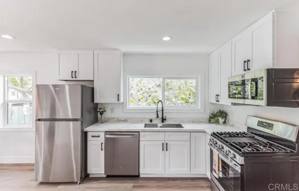 a kitchen with granite countertop a sink stove a refrigerator and white cabinets with wooden floor