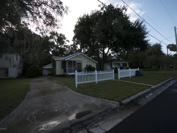 a view of a white house next to a yard with big trees