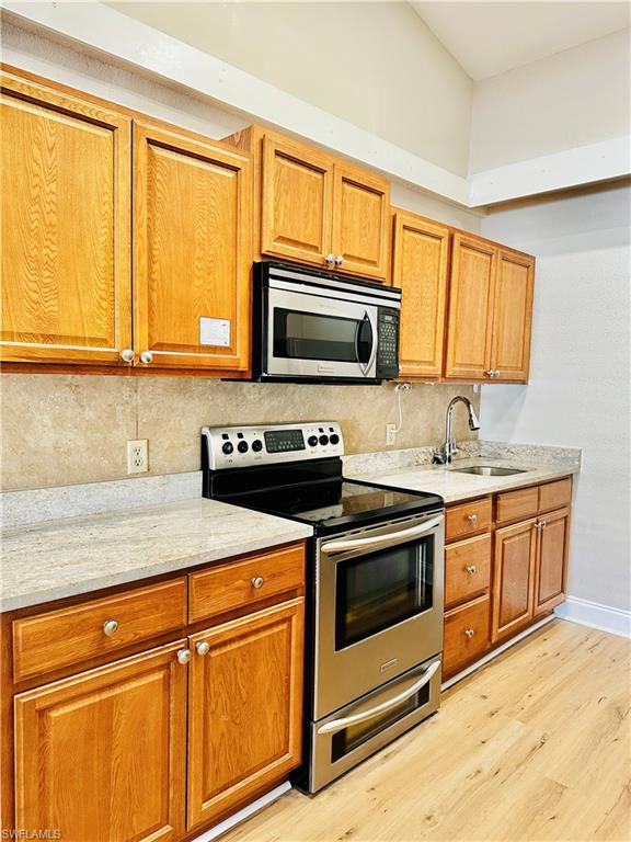 826 Wiggins Pass Road, Unit 310 Naples, FL 34110 - Photo 6 of 18 Kitchen with appliances with stainless steel finishes, light stone countertops, brown cabinets, light wood-style floors, and backsplash