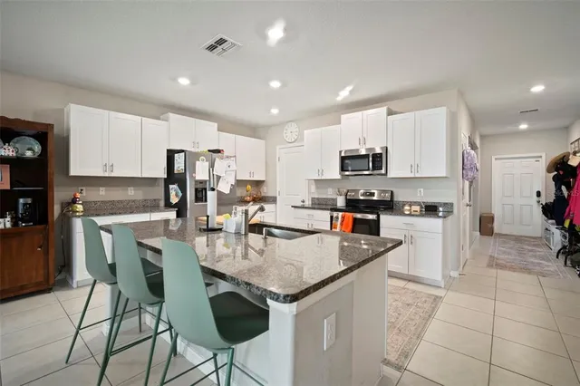a kitchen with stainless steel appliances granite countertop a stove top oven a sink a refrigerator and white cabinets