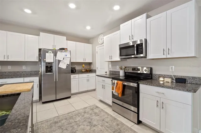 a kitchen with stainless steel appliances granite countertop white cabinets a sink a stove a microwave and a refrigerator