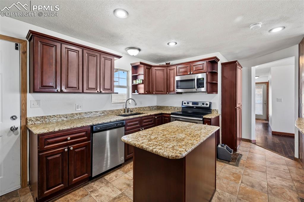 6260 Night Train Lane Yoder, CO 80864 - Photo 14 of 22 Kitchen with a center island, a textured ceiling, appliances with stainless steel finishes, sink, and light tile floors