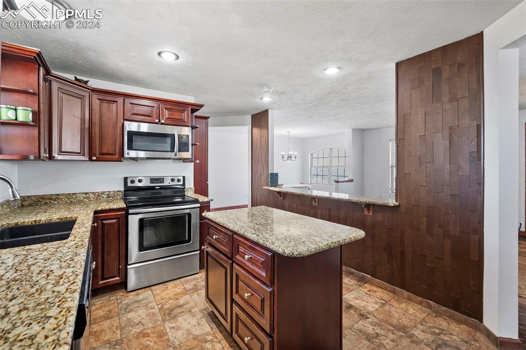 6260 Night Train Lane Yoder, CO 80864 - Photo 15 of 22 Kitchen with light stone countertops, stainless steel appliances, kitchen peninsula, sink, and light tile floors