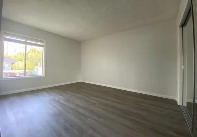a view of an empty room with wooden floor and a window