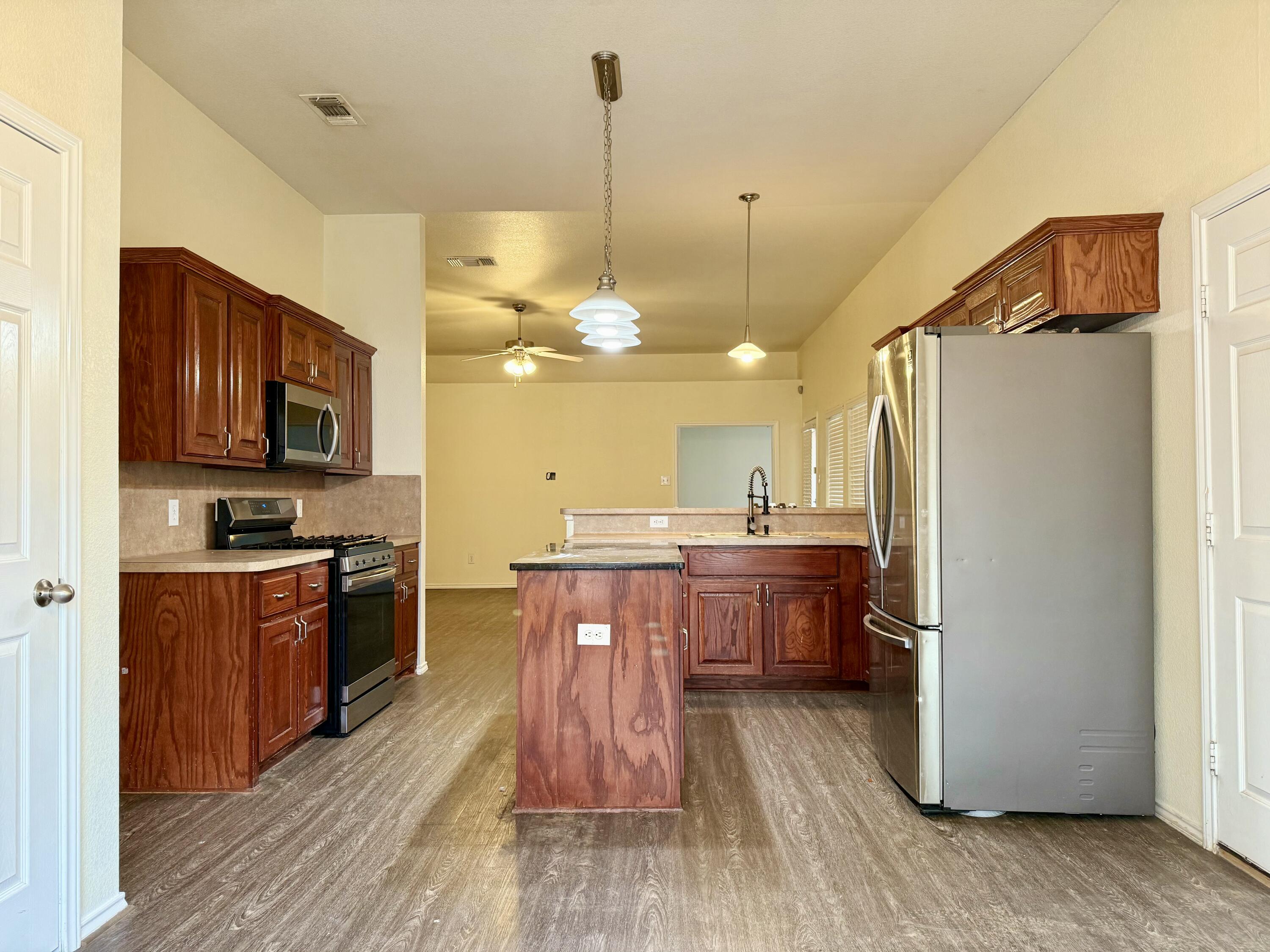 4916 Harvard Drive Lubbock, TX 79416 - Photo 11 of 22 a kitchen with stainless steel appliances granite countertop a refrigerator a stove top oven a sink dishwasher and wooden cabinets with wooden floor
