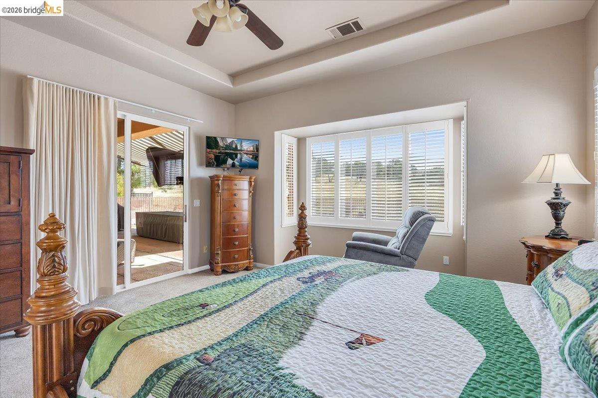 158 Rock Ridge Lane Copperopolis, CA 95228 - Photo 33 of 72 Bedroom featuring a tray ceiling with a ceiling fan, a large window with plantation shutters, and a sliding glass door leading to an outdoor covered area