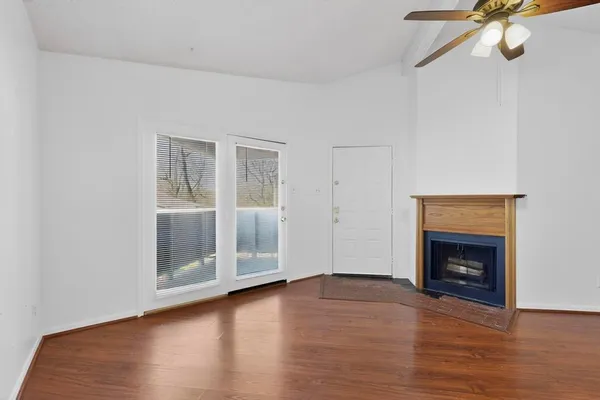 a view of an empty room with wooden floor fireplace and a window