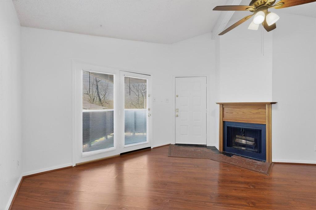 a view of an empty room with wooden floor fireplace and a window