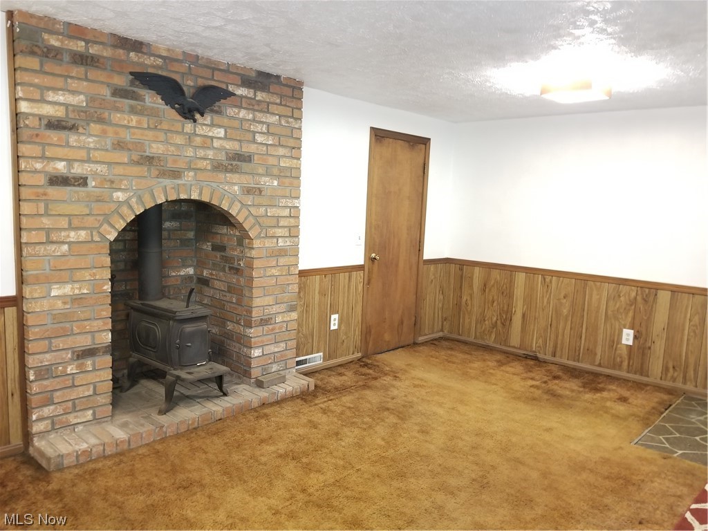 756 Cunningham Road Salem, OH 44460 - Photo 20 of 25 Unfurnished living room with brick wall, wooden walls, a textured ceiling, light carpet, and a wood stove