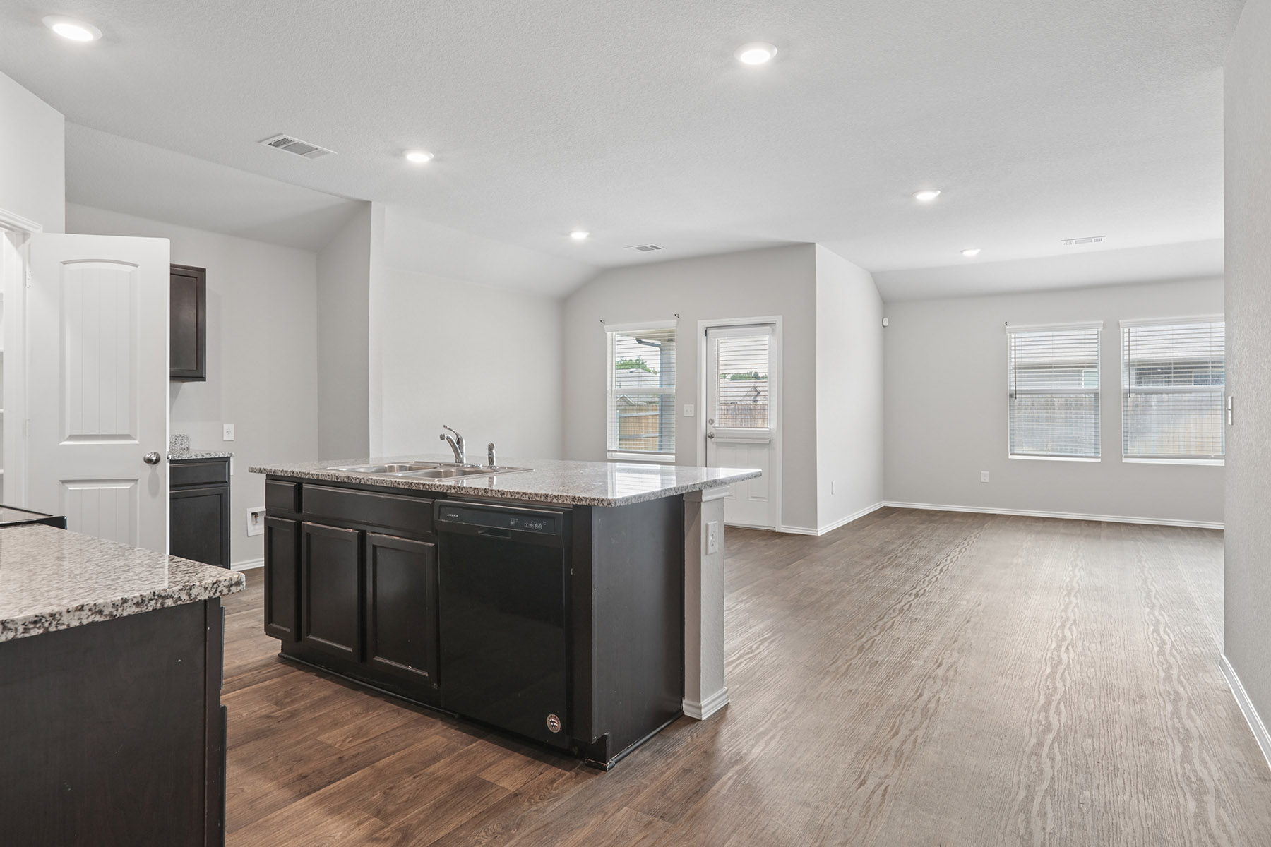 15217 Upland Willow Road Austin, TX 78724 - Photo 12 of 25 Kitchen with light stone countertops, dishwasher, dark wood-style floors, a center island with sink, and recessed lighting
