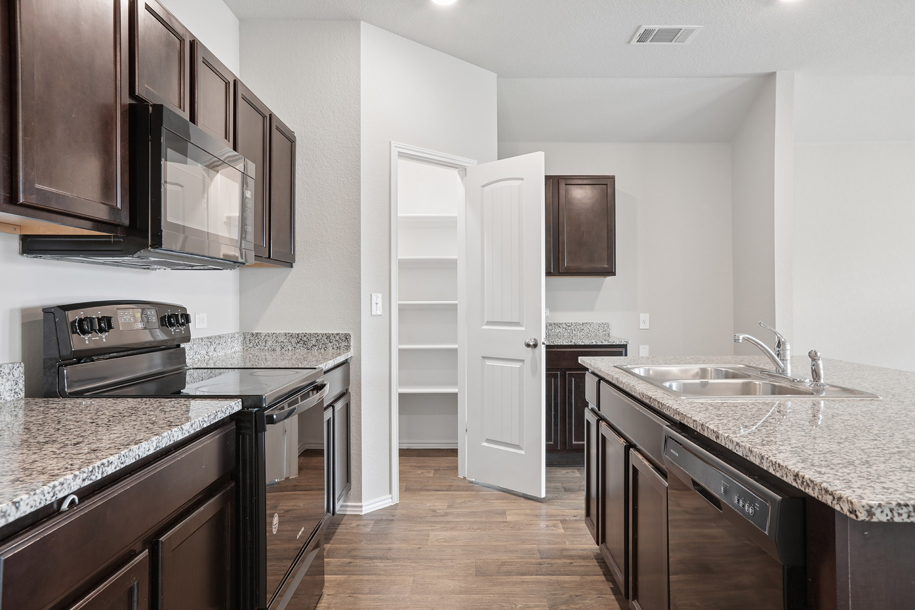 15217 Upland Willow Road Austin, TX 78724 - Photo 13 of 25 Kitchen with black appliances, dark wood finish cabinets, dark wood-type flooring, a kitchen island with sink, and light stone counters