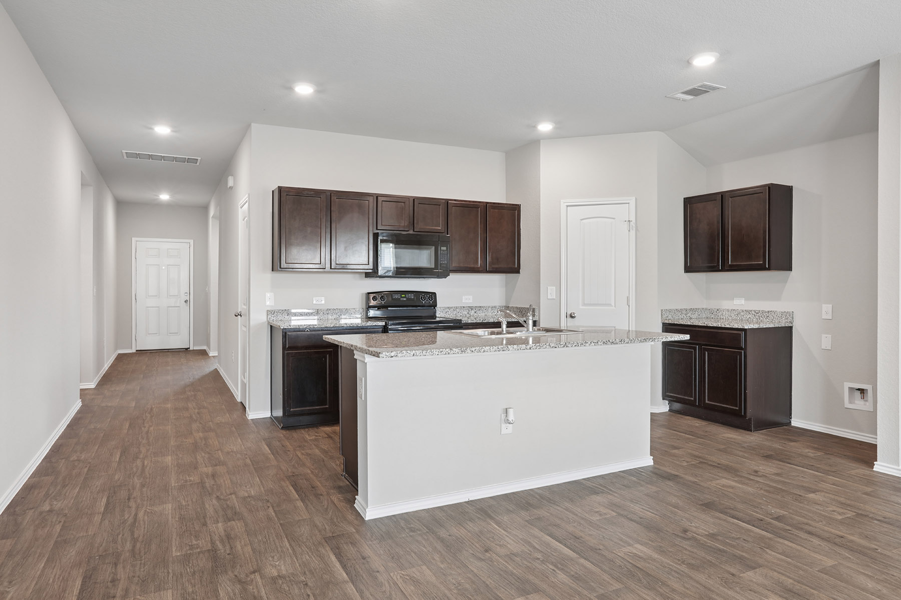 15217 Upland Willow Road Austin, TX 78724 - Photo 14 of 25 Kitchen featuring dark wood finish cabinets, light stone counters, an island with sink, and recessed lighting