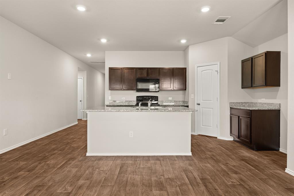 15217 Upland Willow Road Austin, TX 78724 - Photo 16 of 25 Kitchen featuring dark wood finish cabinets, black appliances, light stone counters, an island with sink, and recessed lighting
