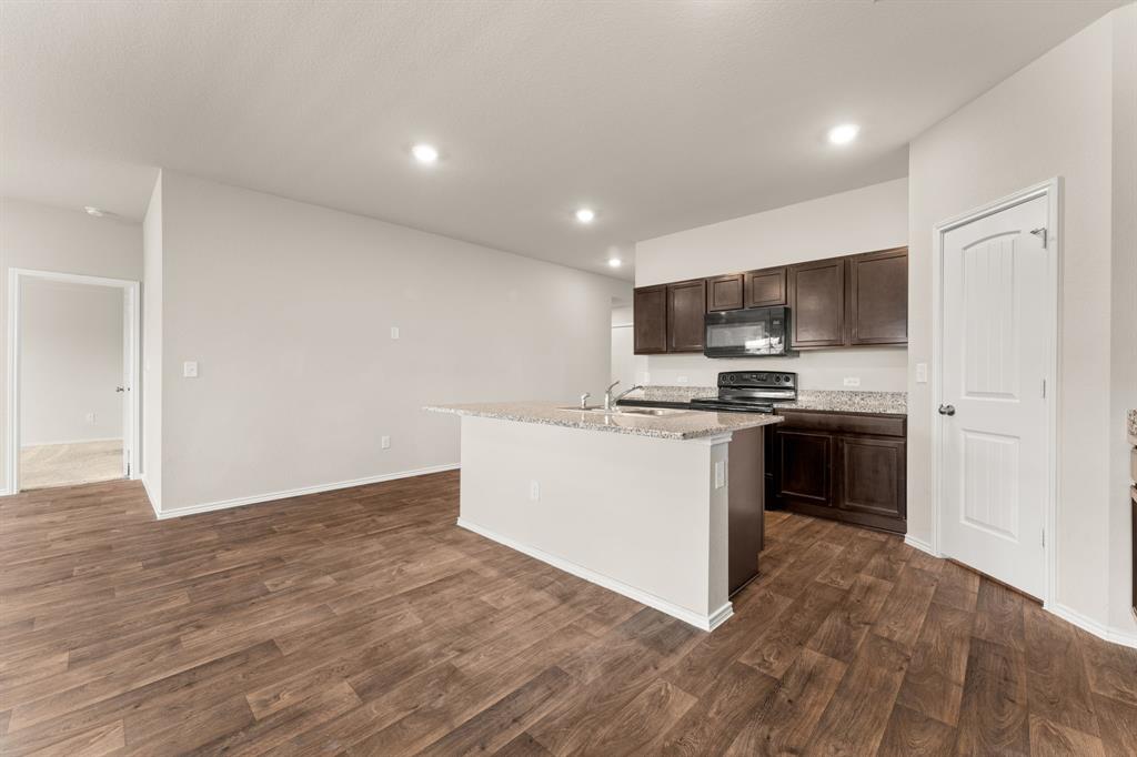 15217 Upland Willow Road Austin, TX 78724 - Photo 17 of 25 Kitchen featuring dark wood finish cabinets, an island with sink, dark wood-style floors, black appliances, and recessed lighting