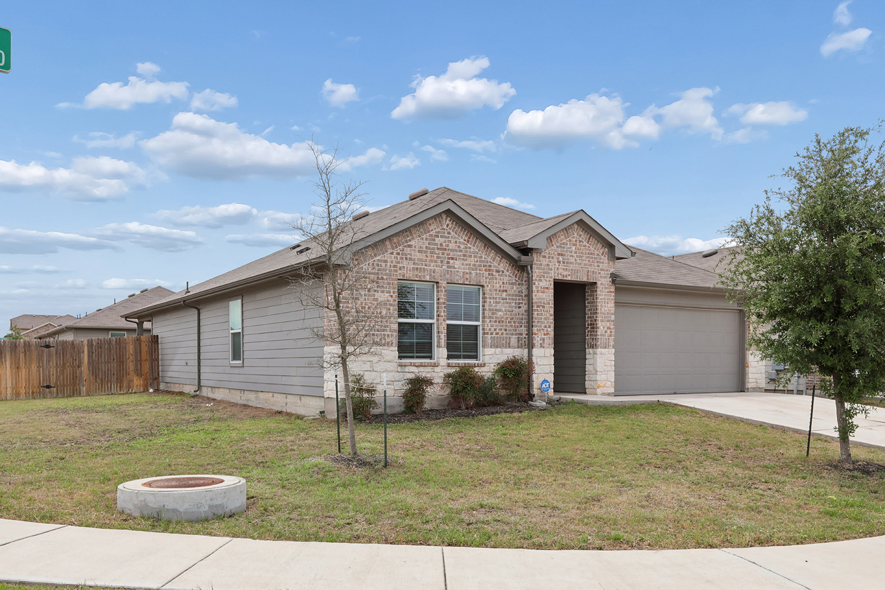 15217 Upland Willow Road Austin, TX 78724 - Photo 4 of 25 Large corner lot with an attached garage, concrete driveway, a fire pit, roof with shingles, and brick siding