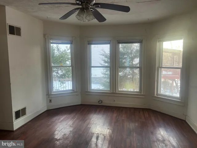 an empty room with wooden floor chandelier fan and windows