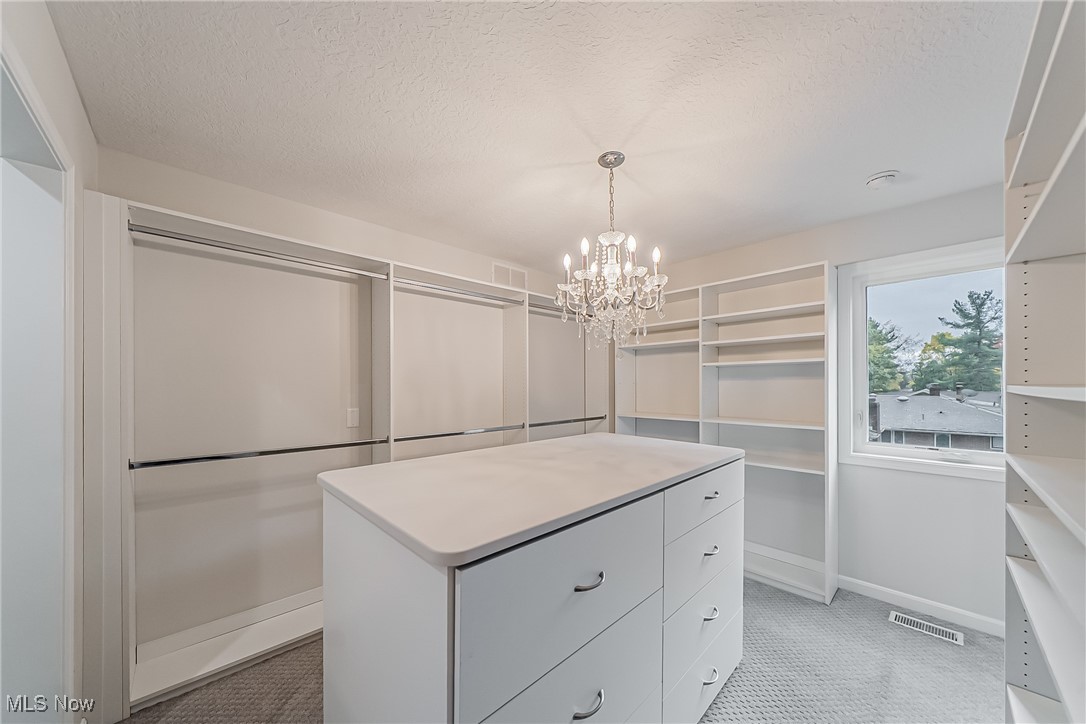 5270 Brainard Road Solon, OH 44139 - Photo 26 of 45 Spacious custom built primary suite closet with built ins, island with storage and window to allow natural light, a chandelier and light carpet