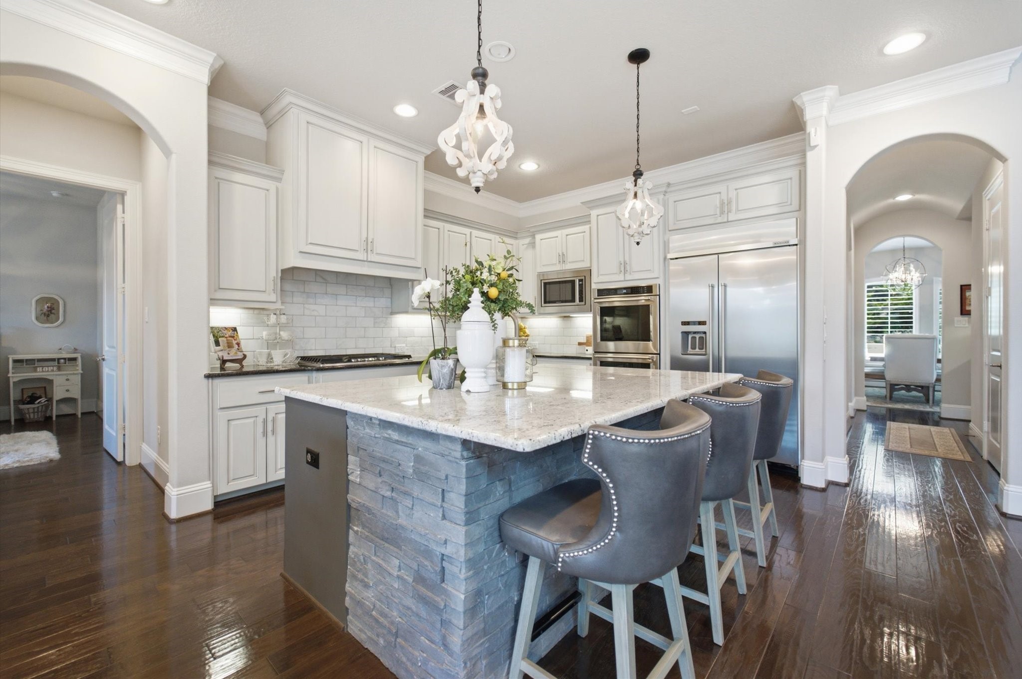 23722 Thortons Park Lane Spring, TX 77389 - Photo 23 of 48 This kitchen features modern elegance with white cabinetry, stainless steel appliances, and a stone-accented island. It includes a breakfast bar with stylish seating, pendant lighting, and dark hardwood floors. Arched doorways lead to adjacent rooms, enhancing the open and inviting space.