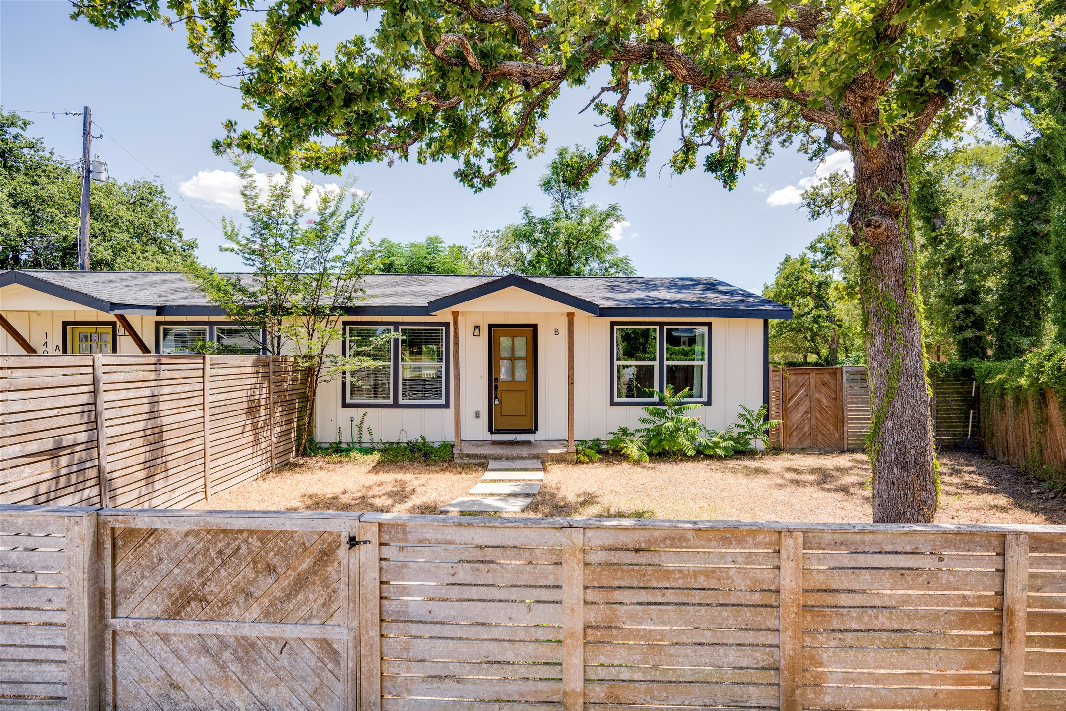 1400 Marcus Place, Unit B Austin, TX 78721 - Photo 5 of 39 A charming cottage facade framed by lush trees and a rustic wood fence provides exceptional curb appeal.