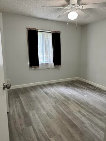 a view of an empty room with wooden floor and fan
