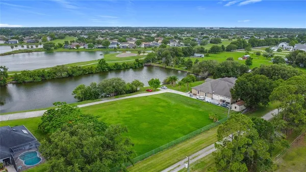 an aerial view of green landscape with trees lake and houses in the back