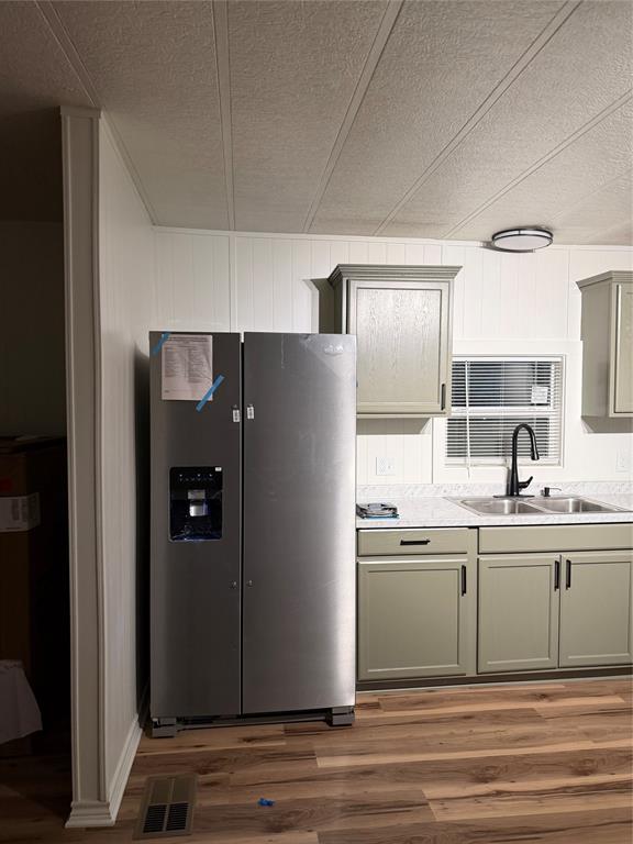 305 West Bryant Street Elm Mott, TX 76640 - Photo 7 of 19 Kitchen with gray cabinetry, fridge, light wood-style flooring, light countertops, and wooden walls