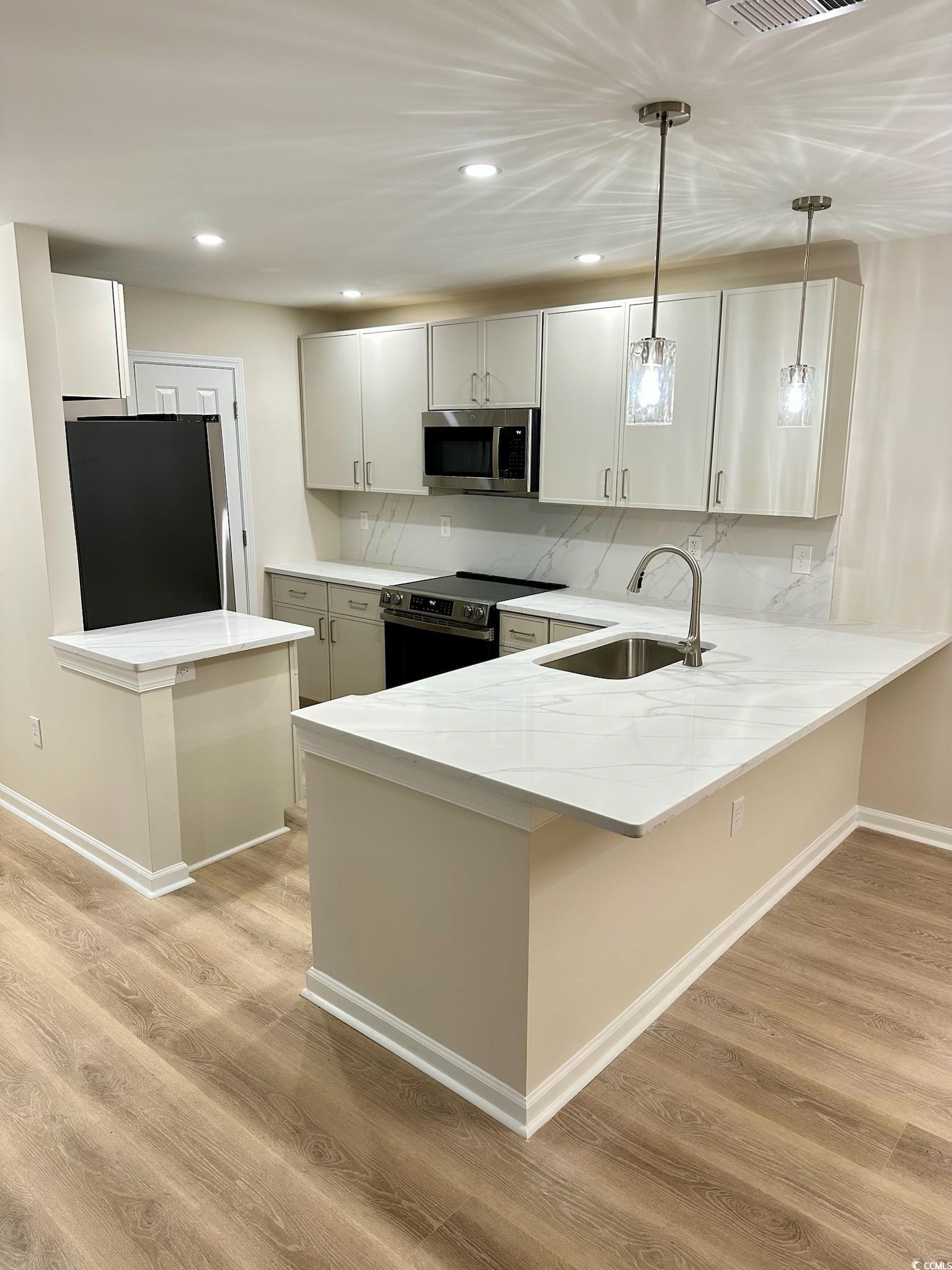 9 Pistachio Loop, Unit D Murrells Inlet, SC 29576 - Photo 4 of 21 Kitchen with a peninsula, decorative light fixtures, a kitchen bar, appliances with stainless steel finishes, and light stone countertops